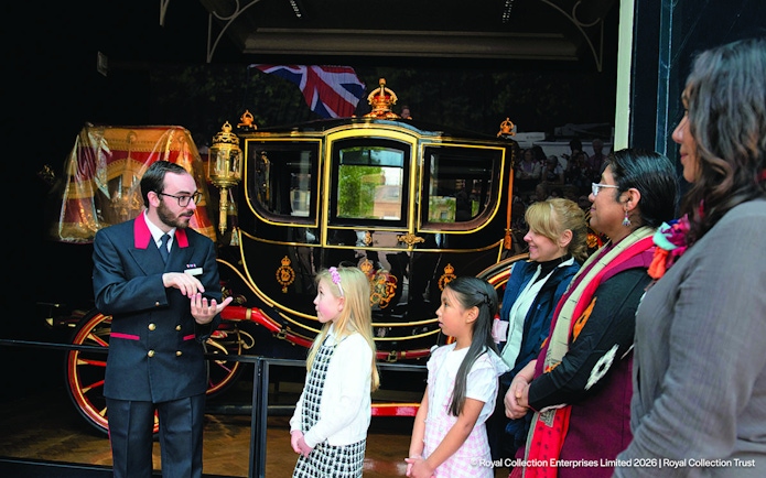 Guide explaining royal carriage to visitors at Royal Mews, London.