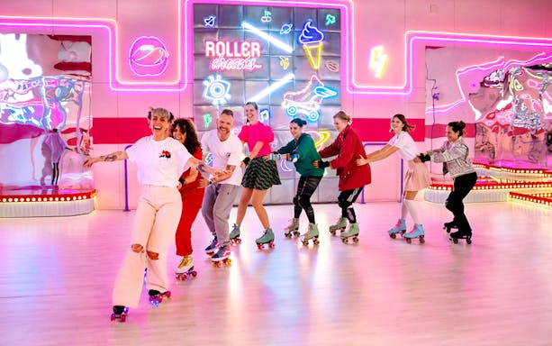 Group roller skating at Amsterdam Roller Dreams rink with neon lights.