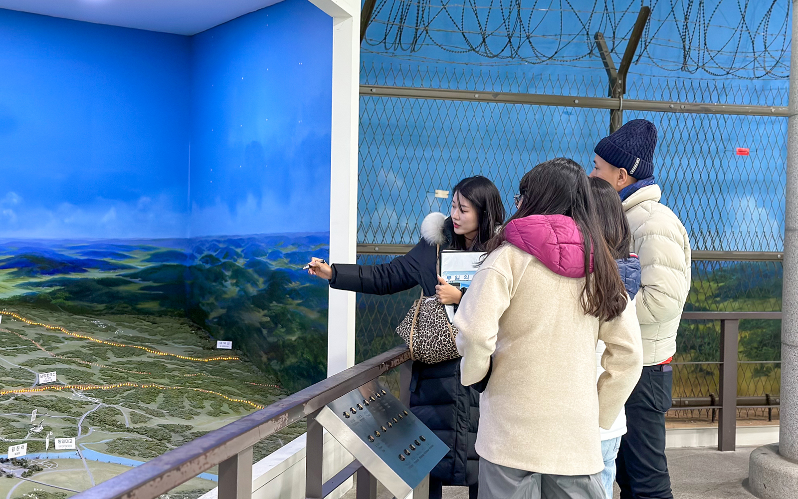 Tour group observing DMZ map display with guide explaining details.