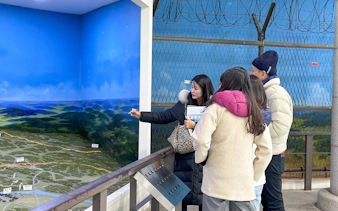 Tour group observing DMZ map display with guide explaining details.