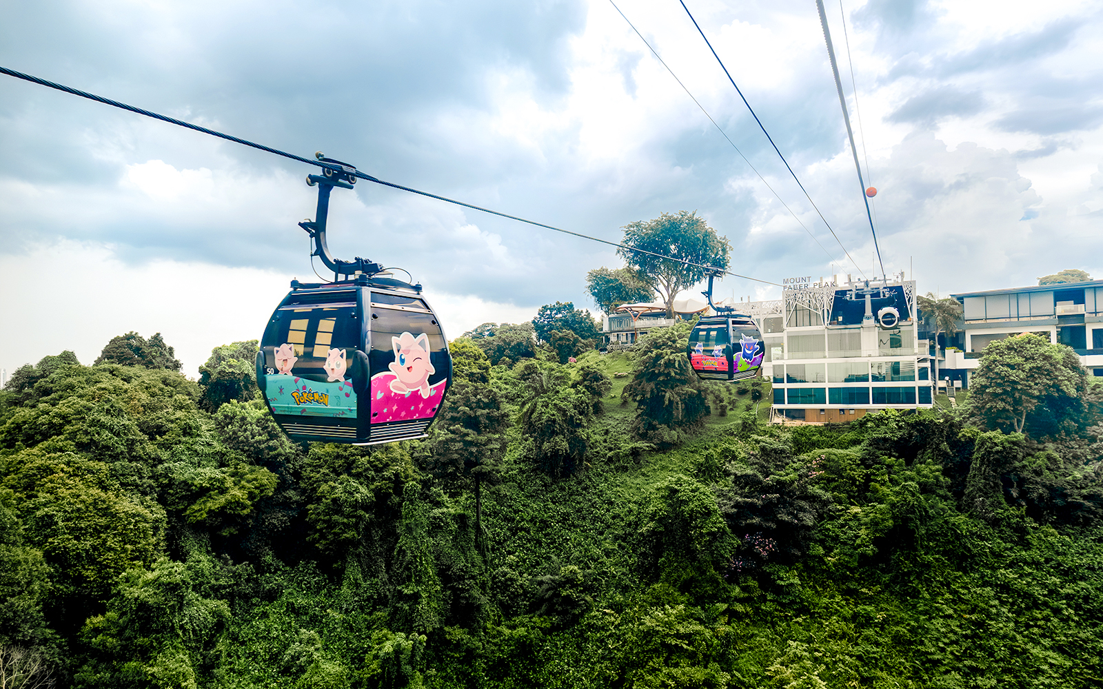 Cable car with Pokémon theme over lush greenery in Sentosa, Singapore.