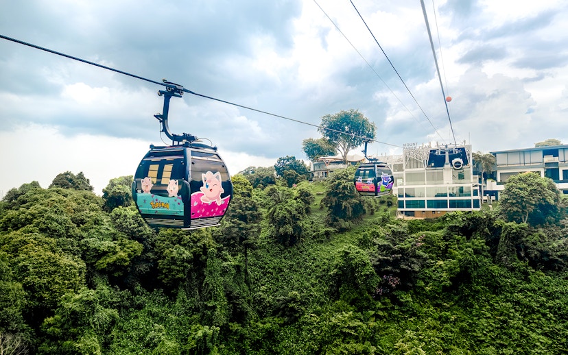 Cable car with Pokémon theme over lush greenery in Sentosa, Singapore.