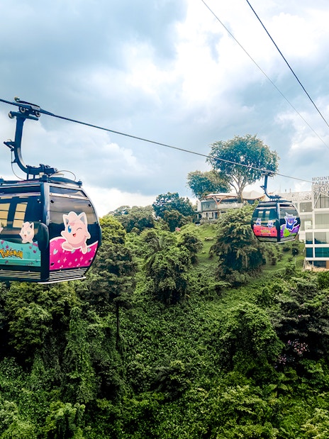 Cable car with Pokémon theme over lush greenery in Sentosa, Singapore.