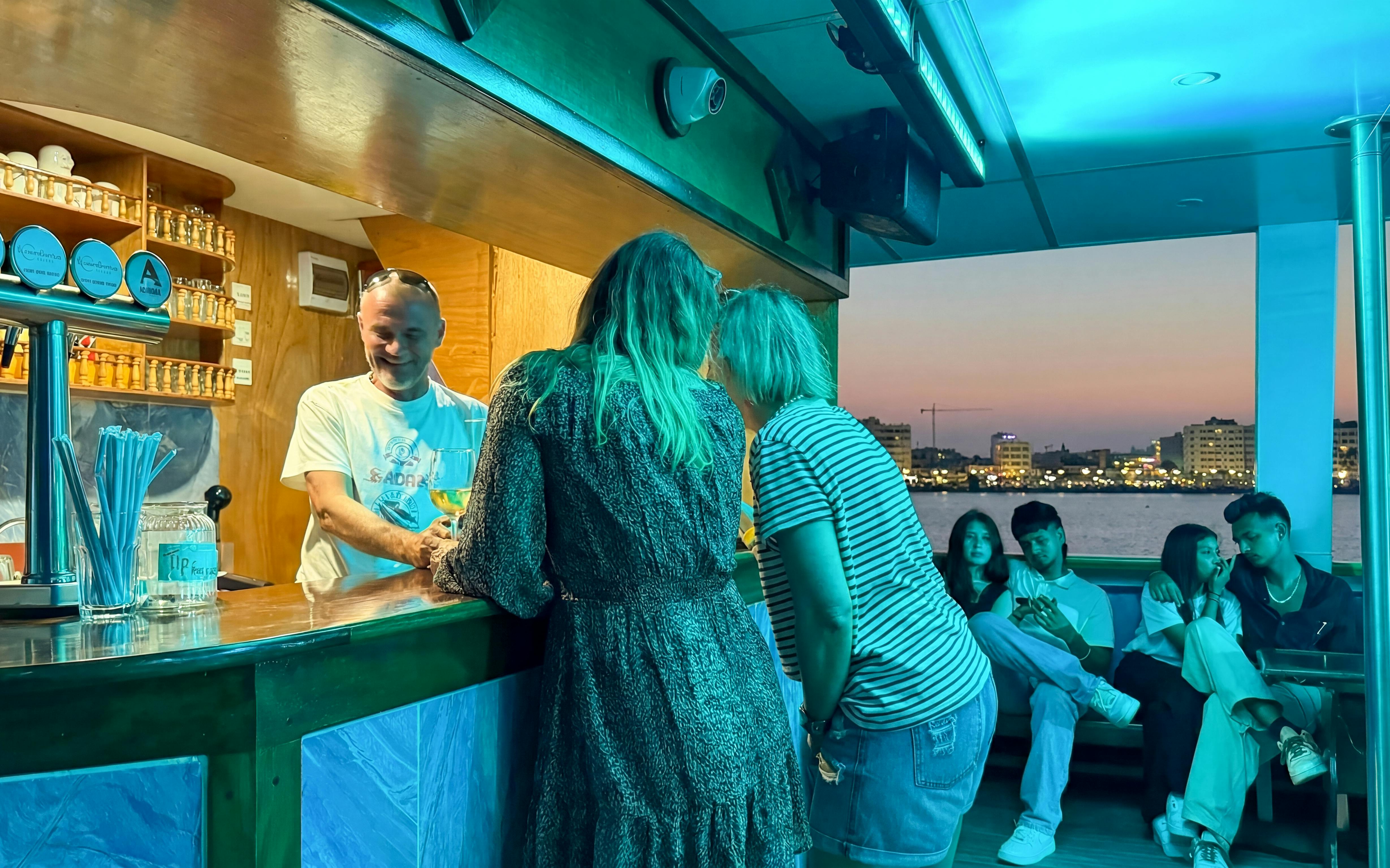 Bartender serving drinks on a sunset cruise from Larnaca with city skyline in the background.