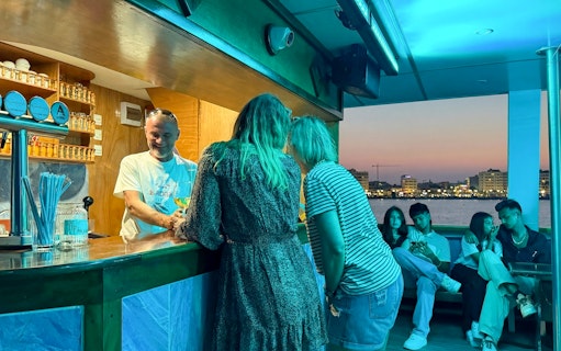 Bartender serving drinks on a sunset cruise from Larnaca with city skyline in the background.