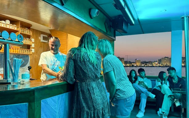 Bartender serving drinks on a sunset cruise from Larnaca with city skyline in the background.