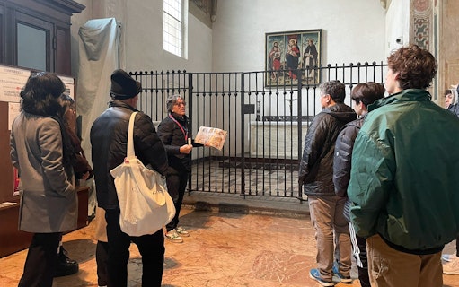 Tour guide explaining a painting to tourists in a historic building.