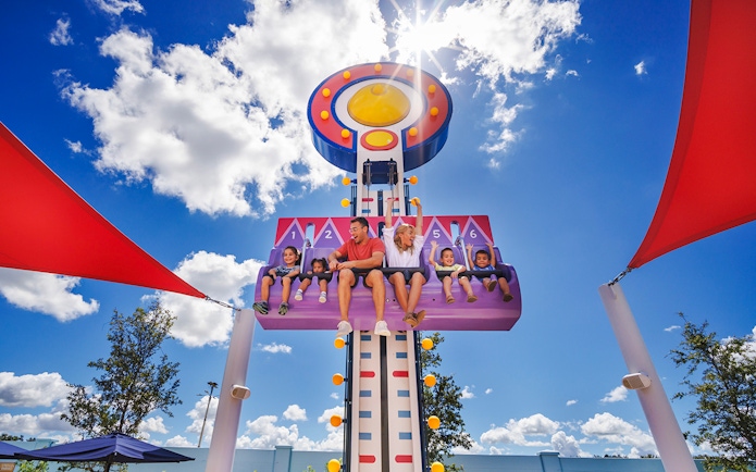 Children and adults on a ride at Peppa Pig Theme Park, Florida under a sunny sky.