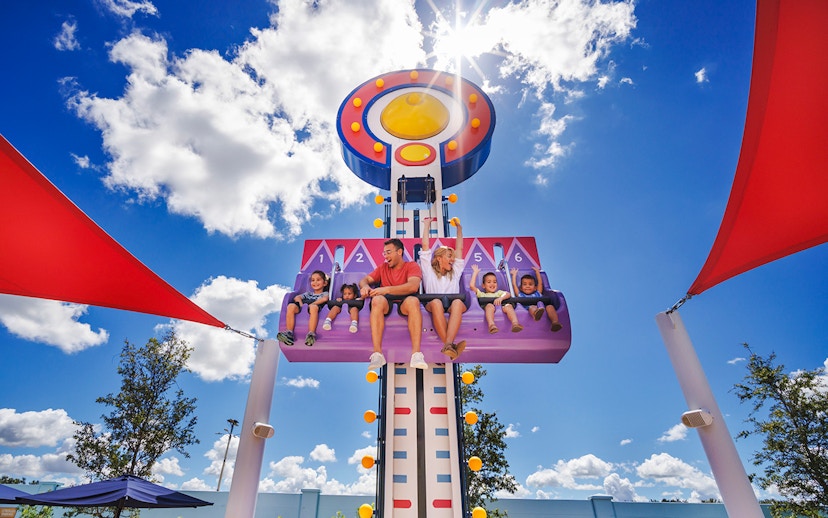 Children and adults on a ride at Peppa Pig Theme Park, Florida under a sunny sky.