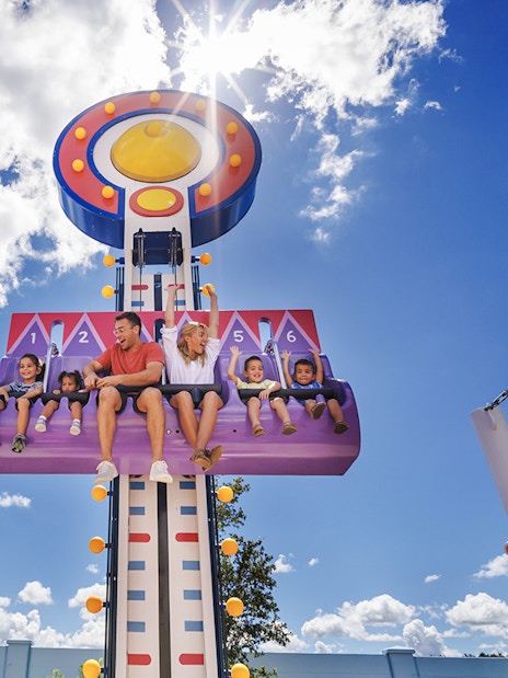 Children and adults on a ride at Peppa Pig Theme Park, Florida under a sunny sky.