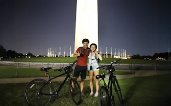 Couple with bikes in front of Washington Monument at night.