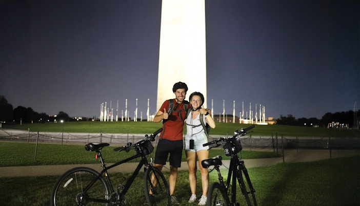 Couple with bikes in front of Washington Monument at night.