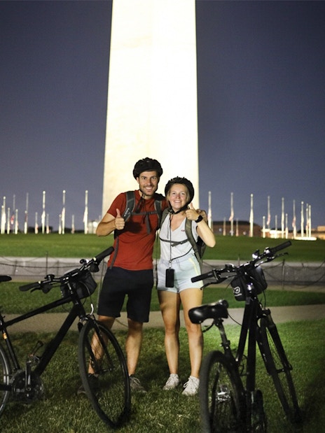 Couple with bikes in front of Washington Monument at night.
