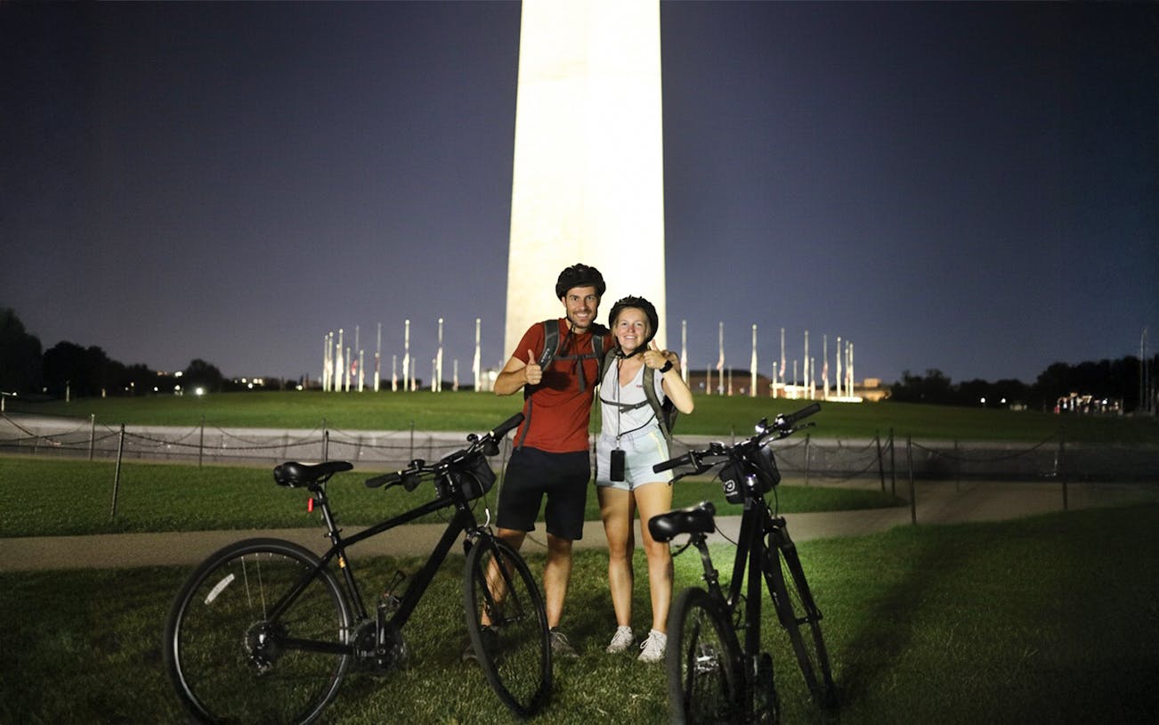 Couple with bikes in front of Washington Monument at night.