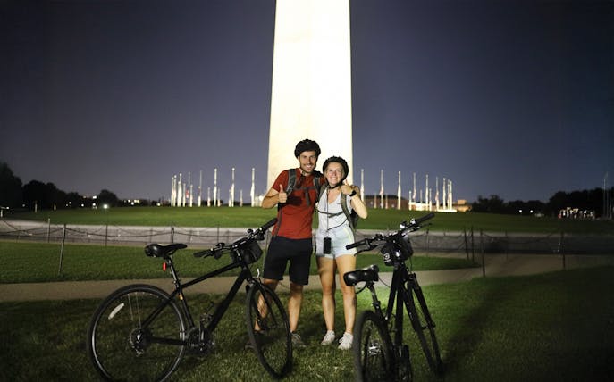Couple with bikes in front of Washington Monument at night.