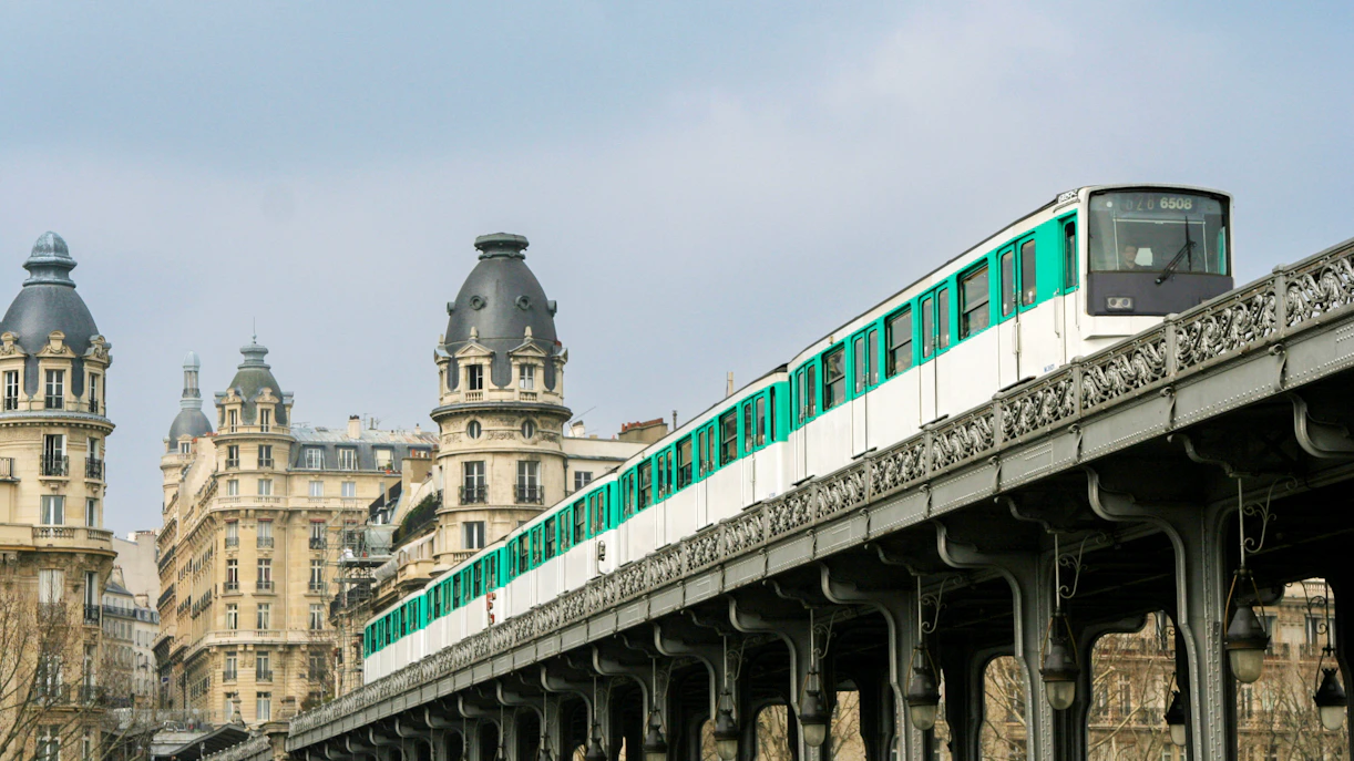 Paris Metro train crossing Bir-Hakeim Bridge with historic buildings in the background.