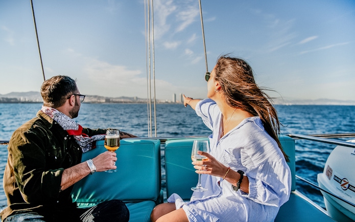 Couple enjoying drinks on a catamaran with Barcelona skyline in the background.
