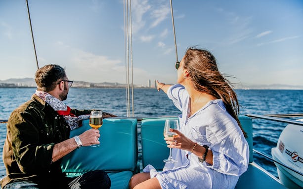 Couple enjoying drinks on a catamaran with Barcelona skyline in the background.