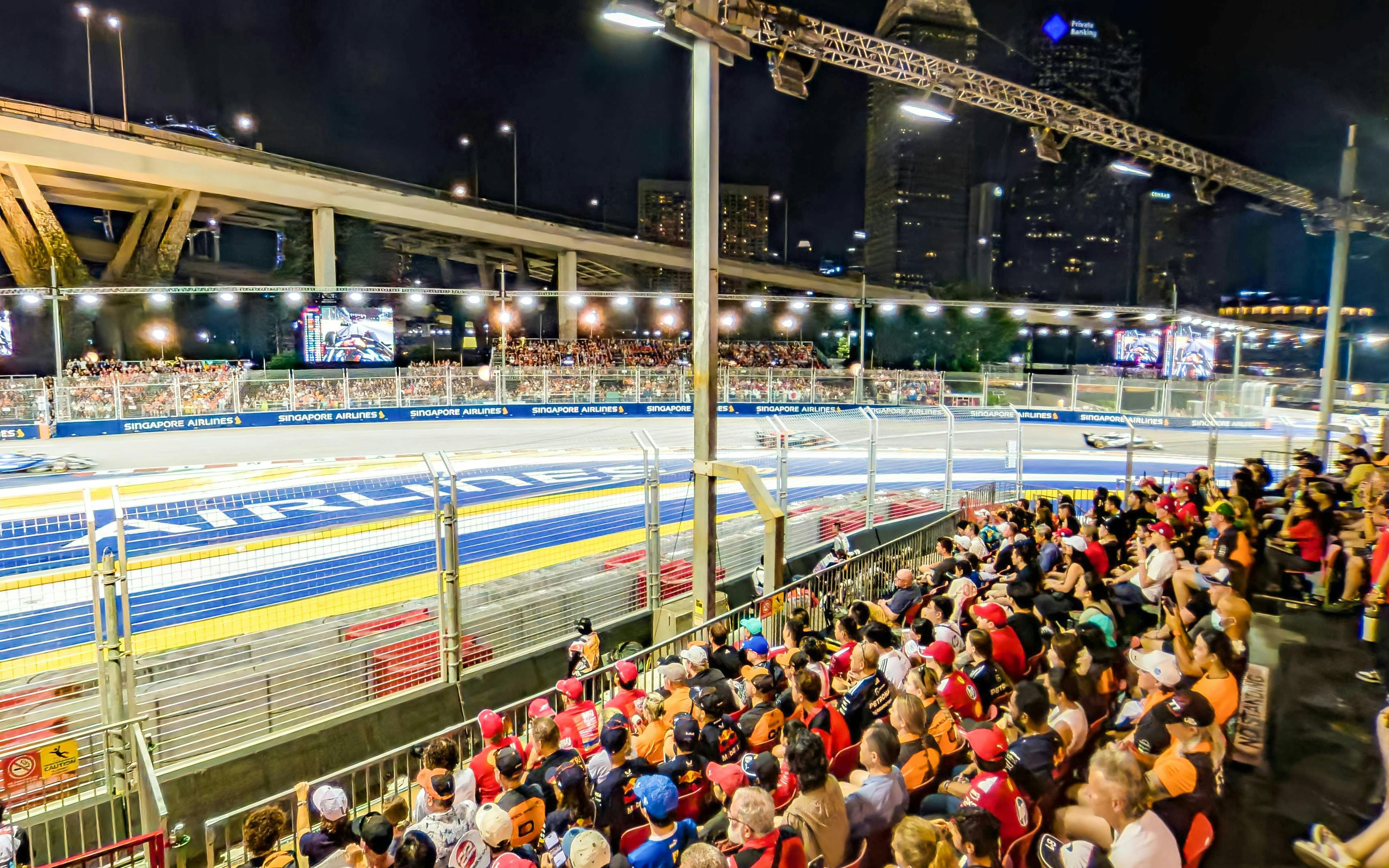 Crowd watching Formula 1 race at night, Singapore Grand Prix track view.