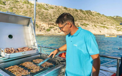 Tourist grilling meat on a catamaran with coastal view in the background.