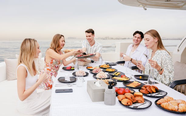 Visitors dining on a cruise in Dubai with a spread of pastries and cold cuts.