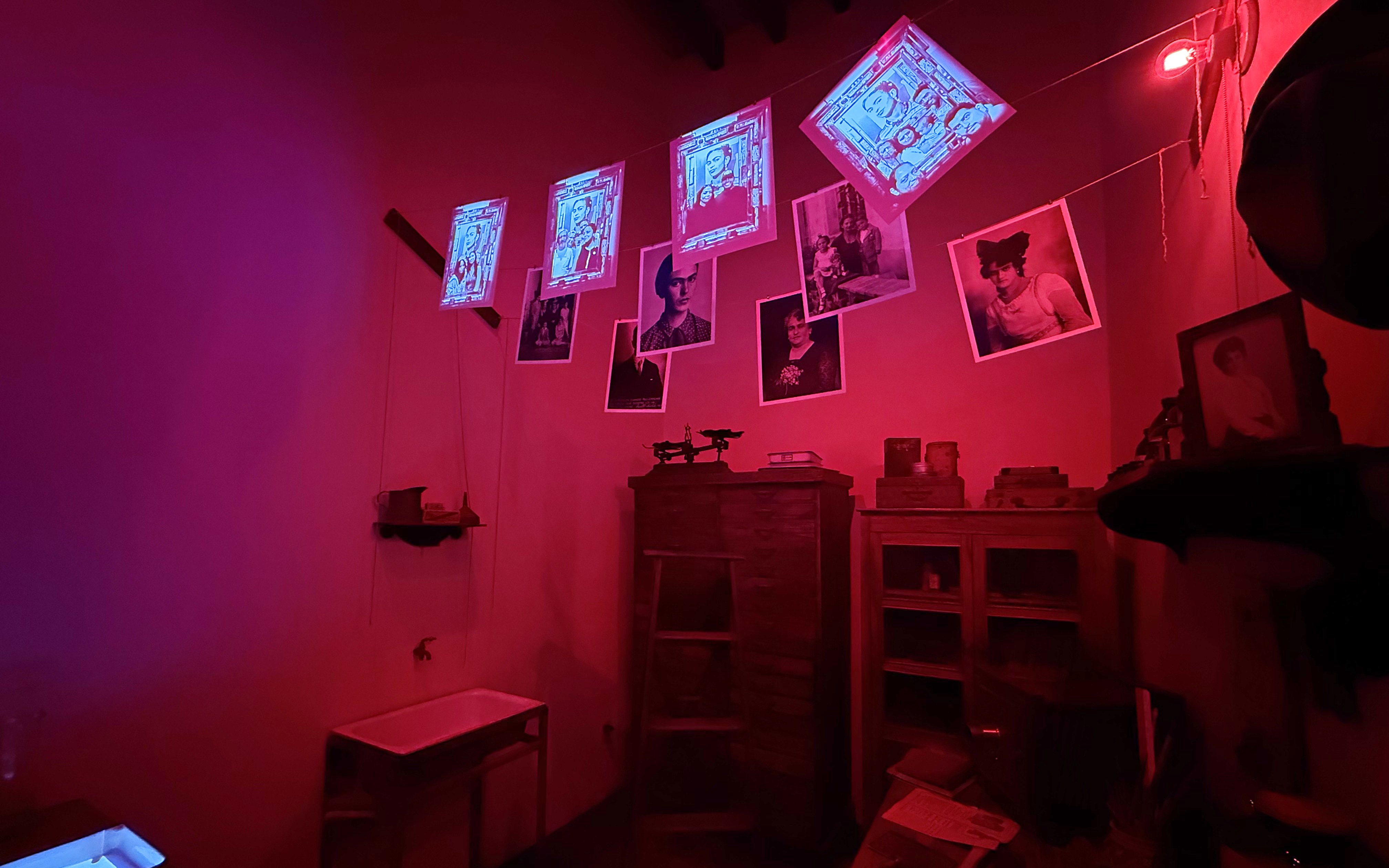 Frida Kahlo Museum room with red lighting, displaying photos and artwork.