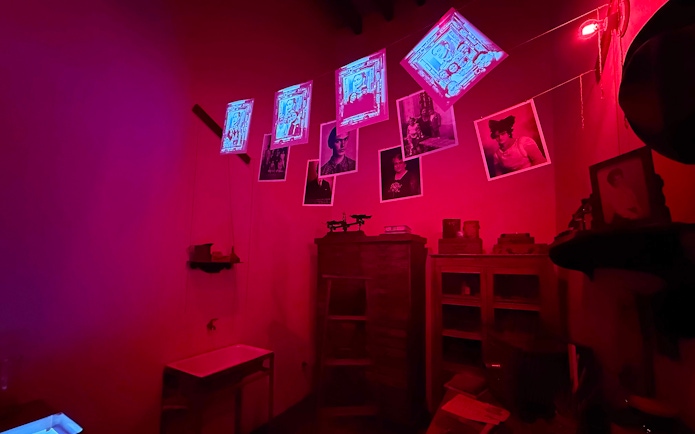 Frida Kahlo Museum room with red lighting, displaying photos and artwork.