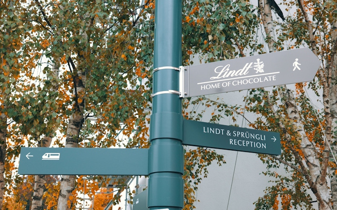 Signpost directing to Lindt Chocolate Museum and reception amidst autumn trees.