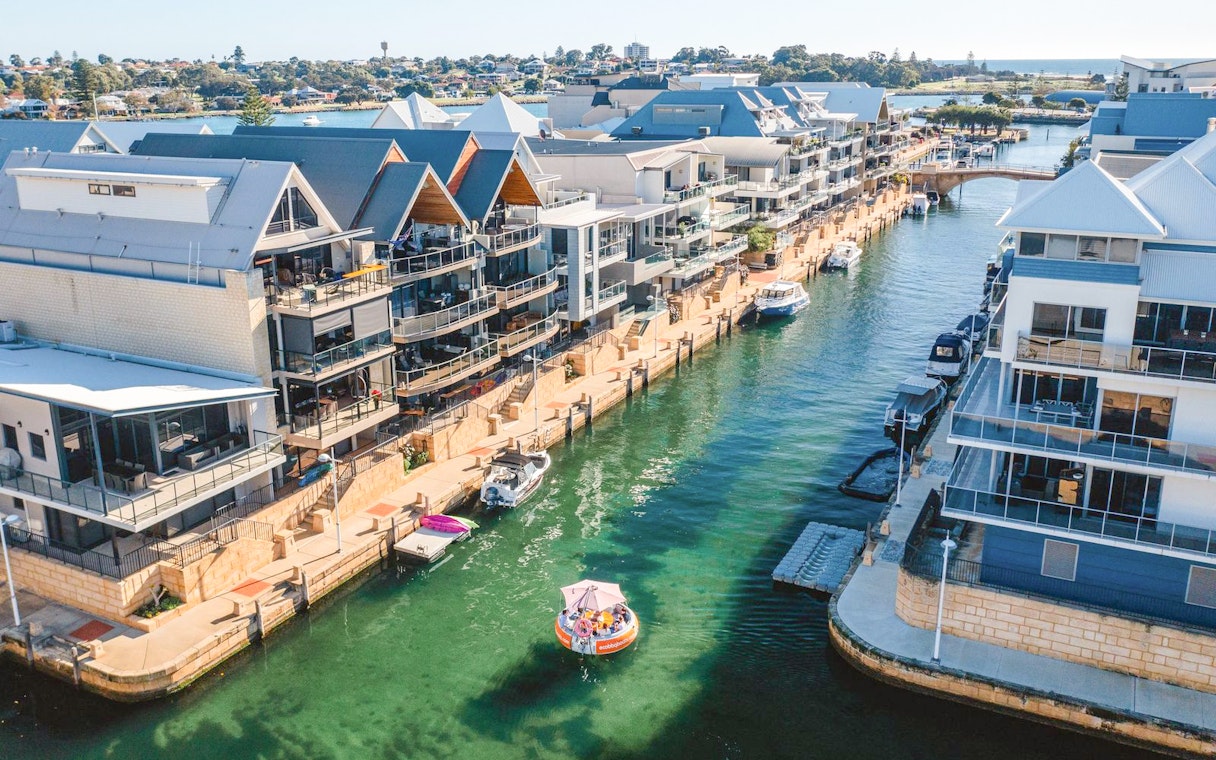 Group enjoying BBQ boat ride in Mandurah canal, surrounded by waterfront homes.
