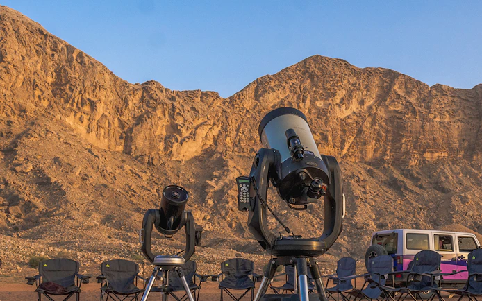 Telescopes set up for stargazing in Mleiha desert with rocky landscape in the background.