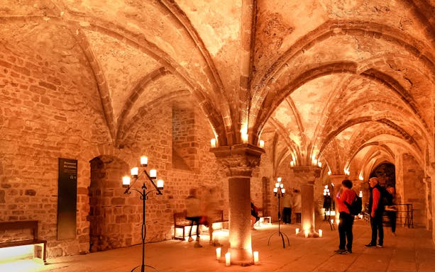 Visitors exploring candlelit arches inside Mont-Saint-Michel Abbey at night.