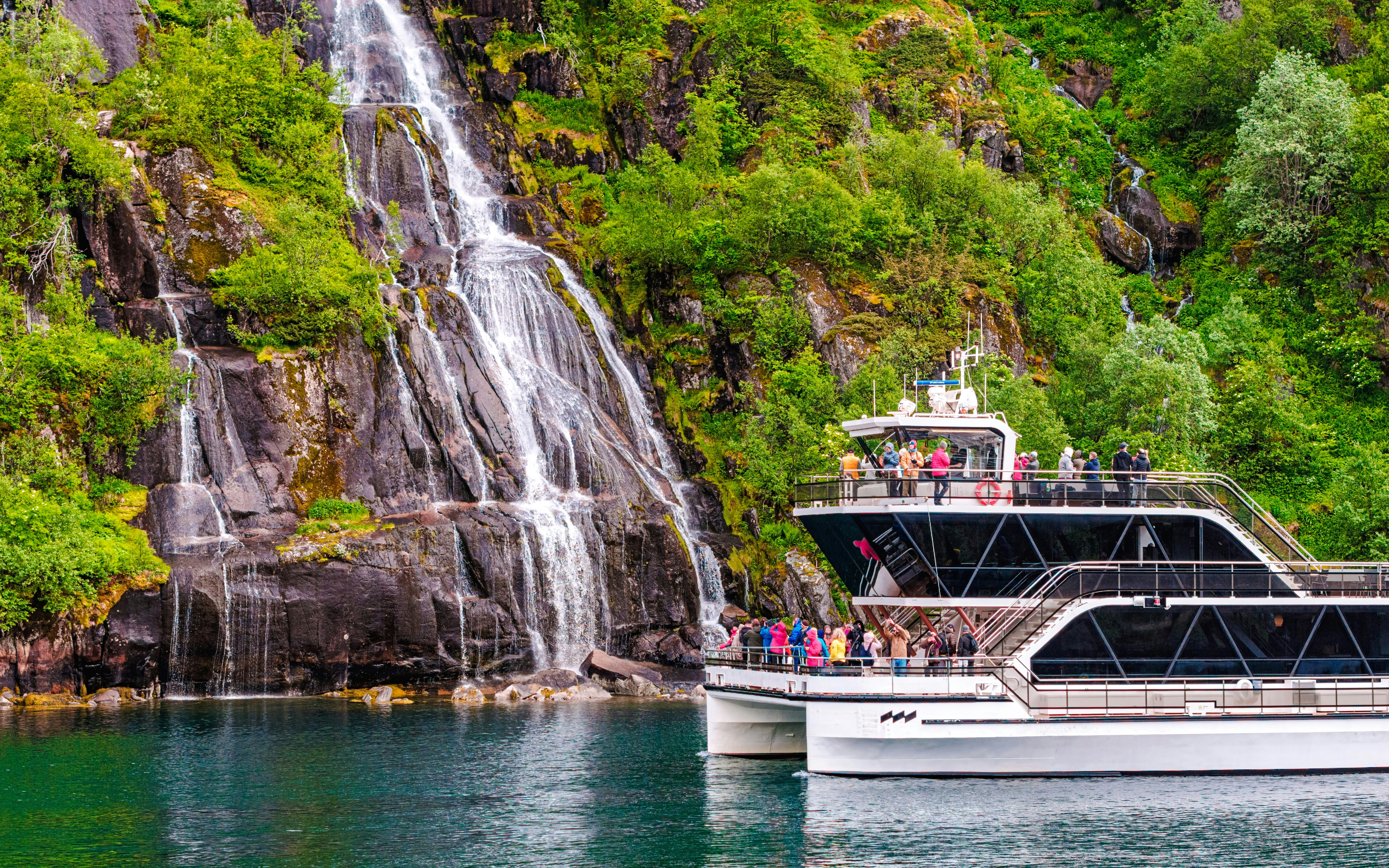 Cruise boat near Whiskey Waterfall in Lysefjord, Stavanger, with tourists on deck.