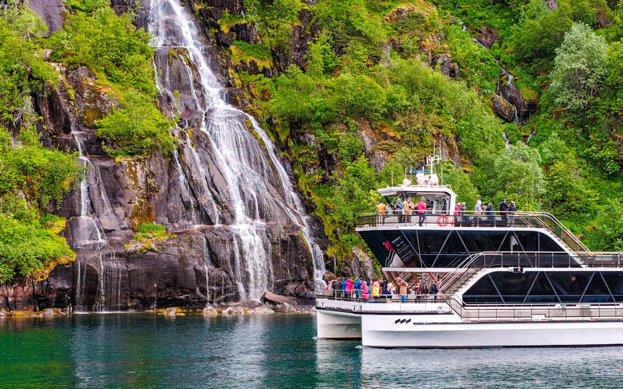 Cruise boat near Whiskey Waterfall in Lysefjord, Stavanger, with tourists on deck.