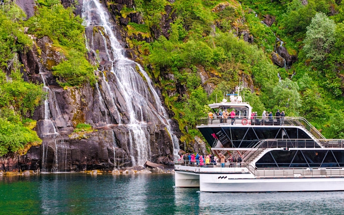 Cruise boat near Whiskey Waterfall in Lysefjord, Stavanger, with tourists on deck.