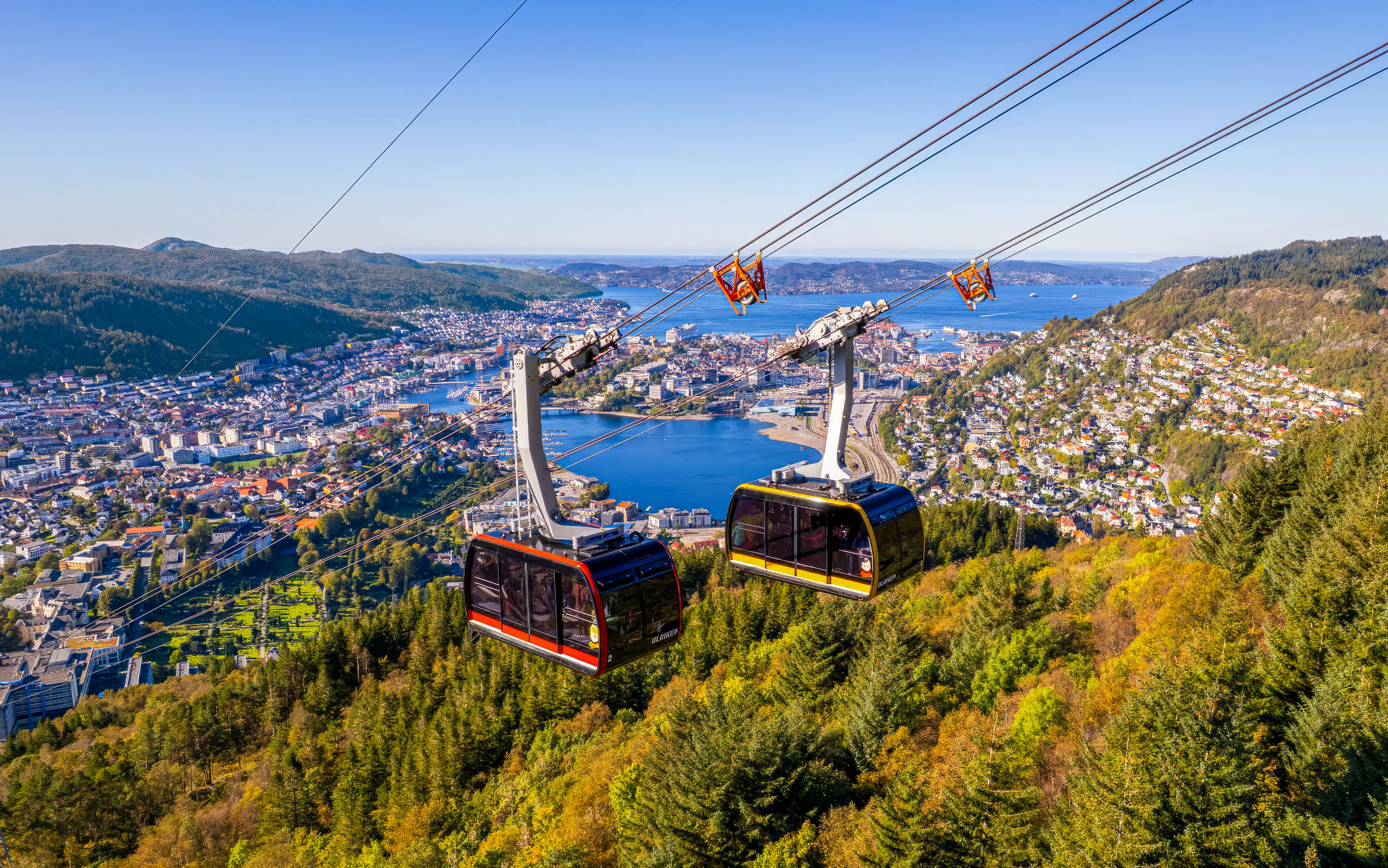 Ulriken cable cars ascending over Bergen, Norway with city and fjord views.