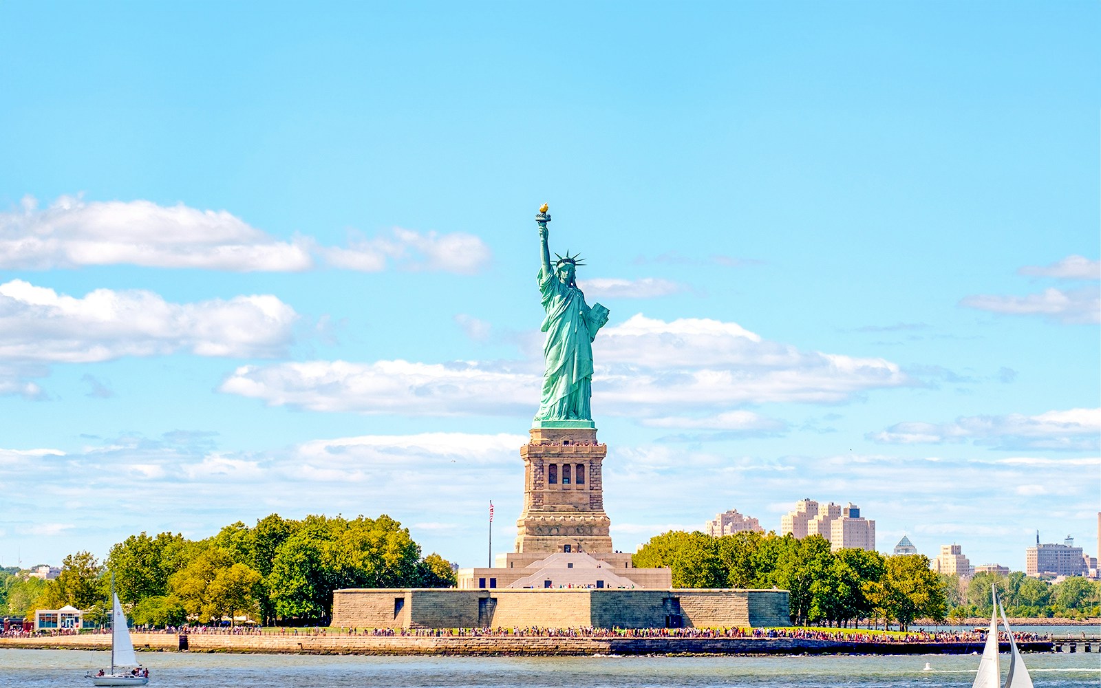 Tourists enjoying a sunny day trip at the Statue of Liberty in New York, USA, with a clear view of the iconic landmark