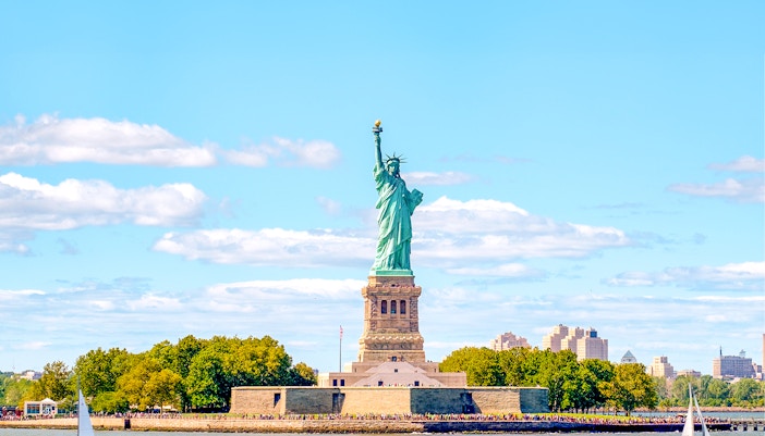 Tourists enjoying a sunny day trip at the Statue of Liberty in New York, USA, with a clear view of the iconic landmark