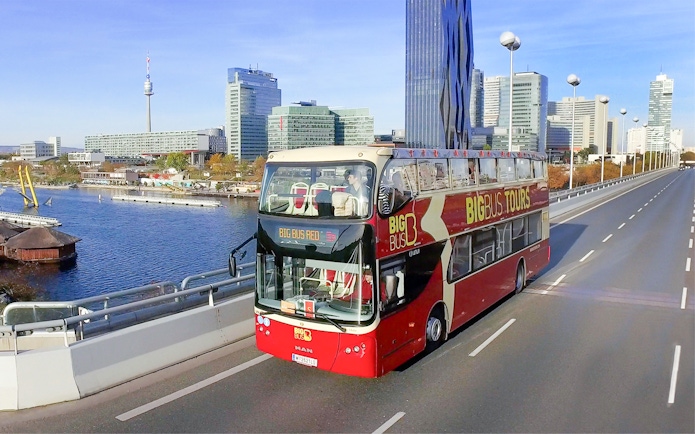 Big Bus tour in Vienna with city skyline and Danube River in the background.