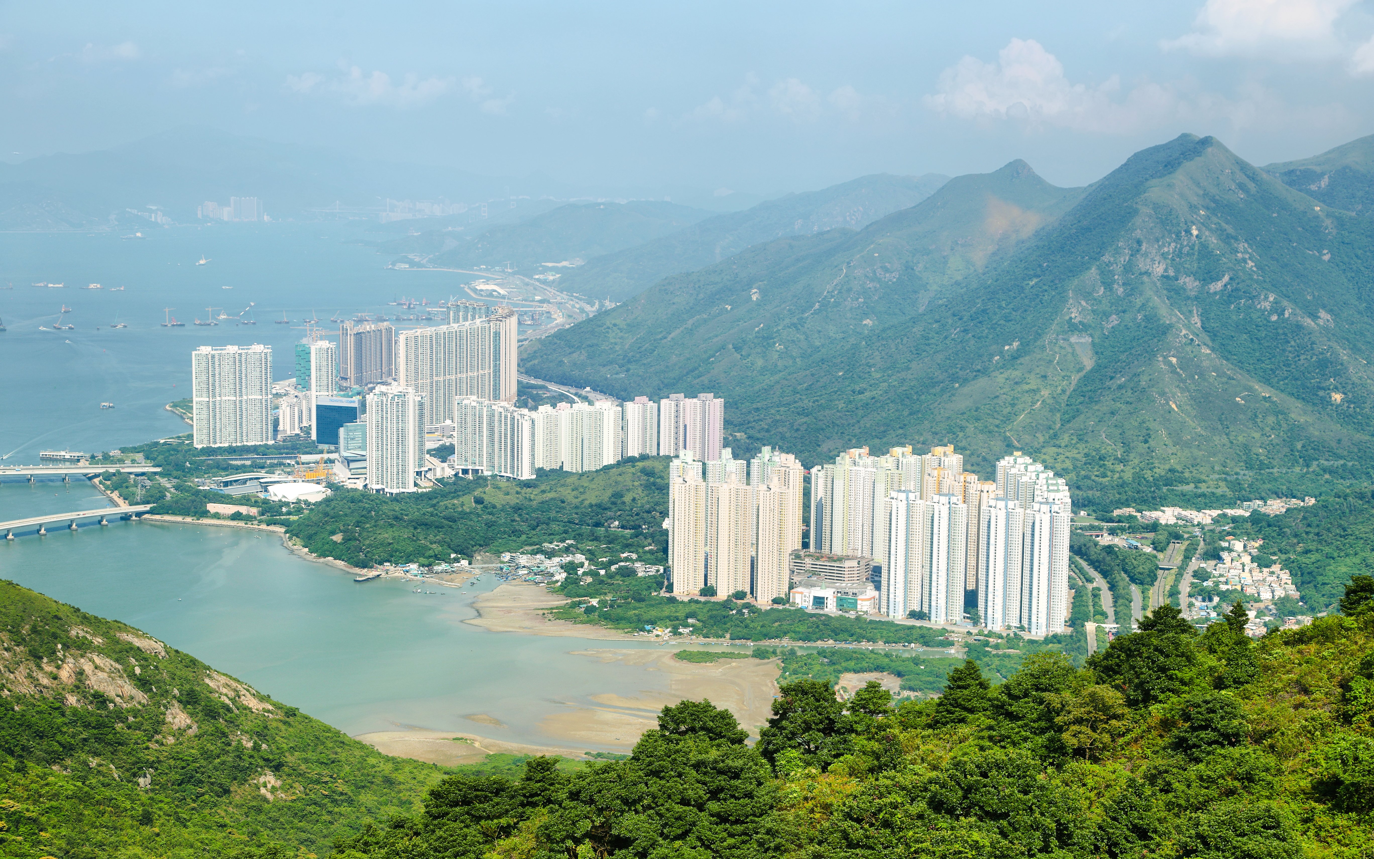 Aerial view of skyscrapers on Lantau Island with surrounding mountains and water.