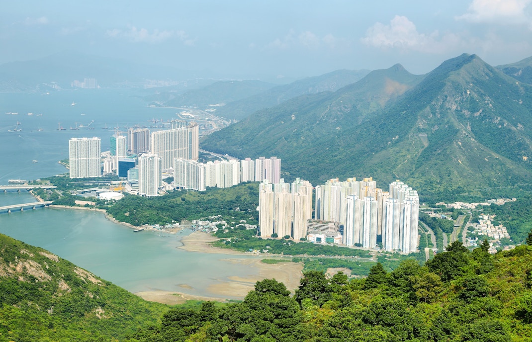Aerial view of skyscrapers on Lantau Island with surrounding mountains and water.