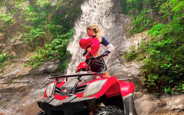 ATV rider in Ubud, Bali, near a waterfall surrounded by lush greenery.