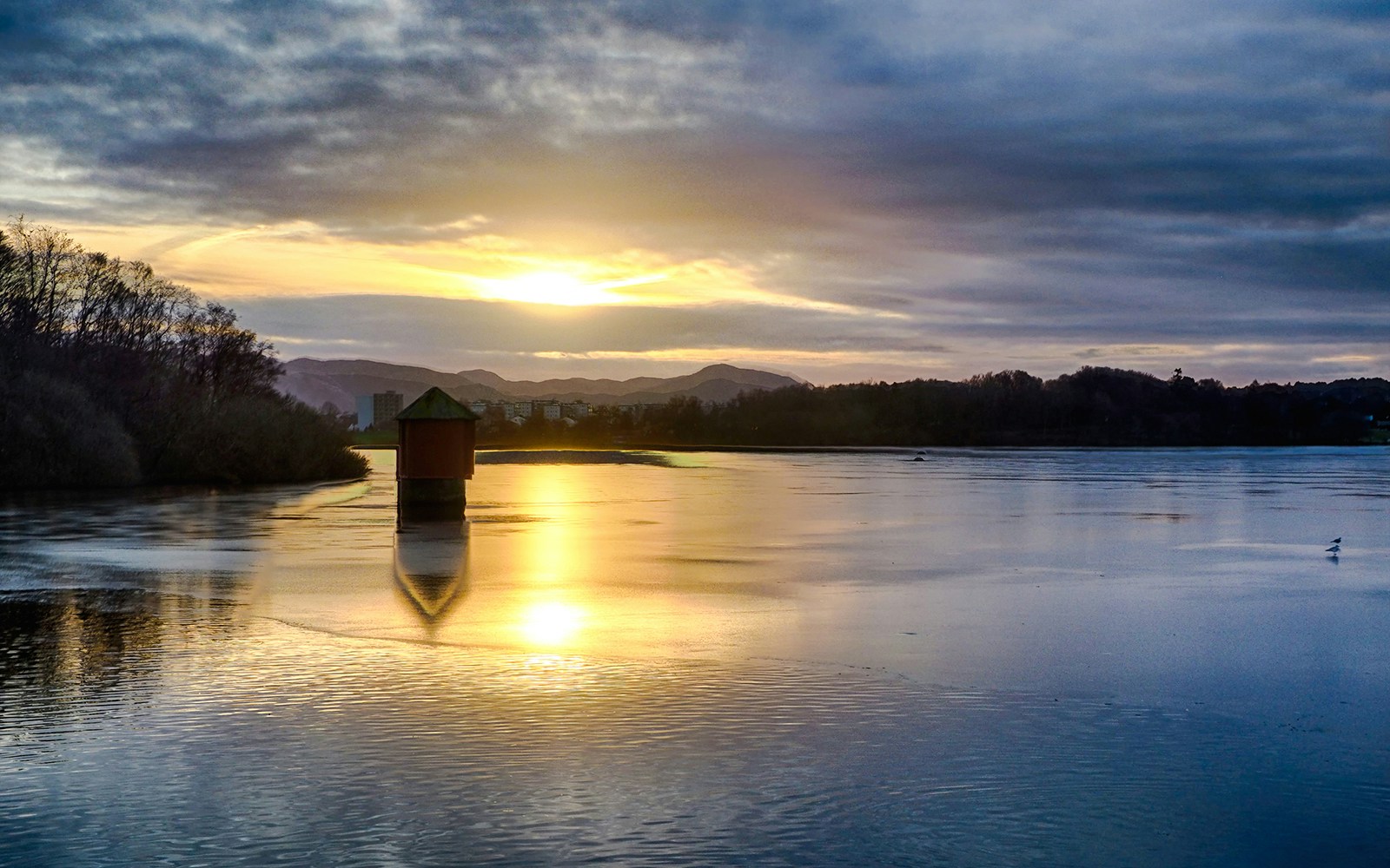 Sunset over Mosvanns-Park lake in Stavanger with a small structure reflecting on the water.