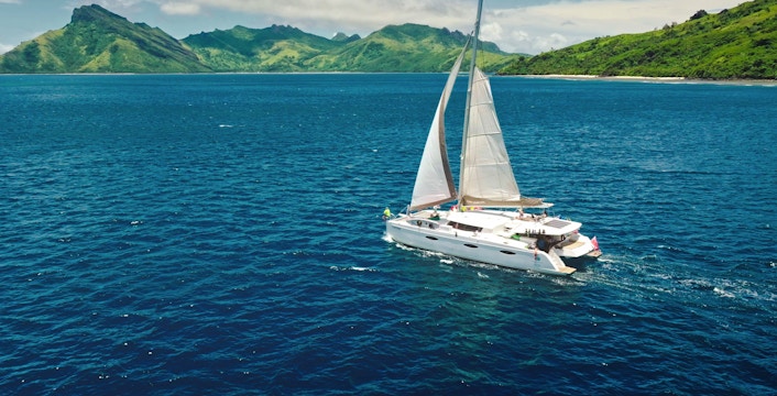 Sailing catamaran near Kuata Island, Fiji, with lush green hills in the background.