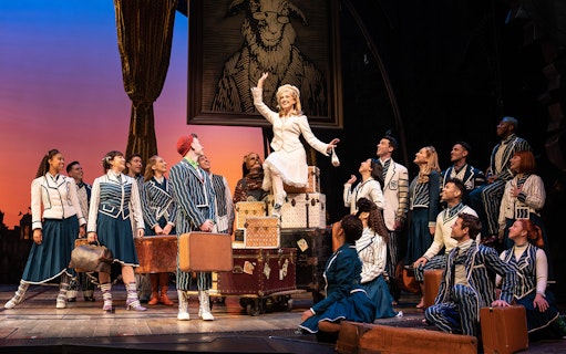 Cast of Wicked musical performing on stage with luggage and costumes.