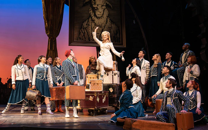 Cast of Wicked musical performing on stage with luggage and costumes.