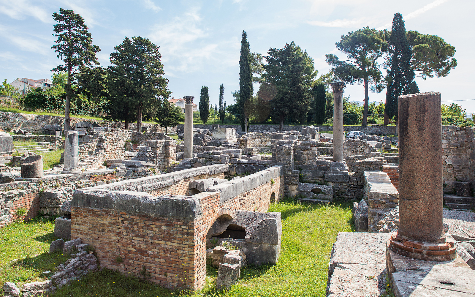 Ancient ruins of Salona with stone columns and walls surrounded by trees.