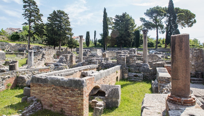 Ancient ruins of Salona with stone columns and walls surrounded by trees.