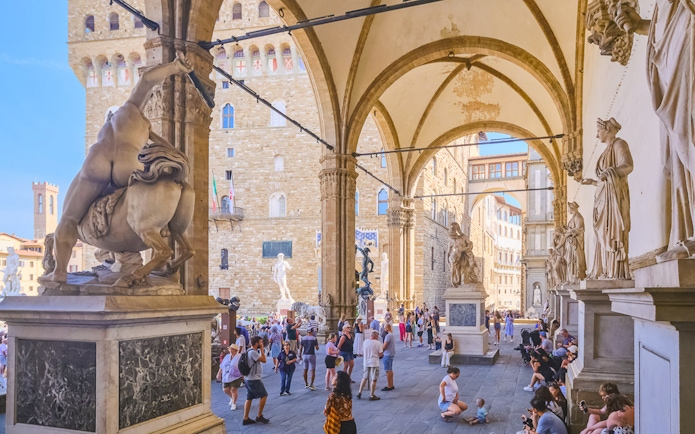 Tourists exploring statues at Loggia dei Lanzi near Palazzo Vecchio, Florence.