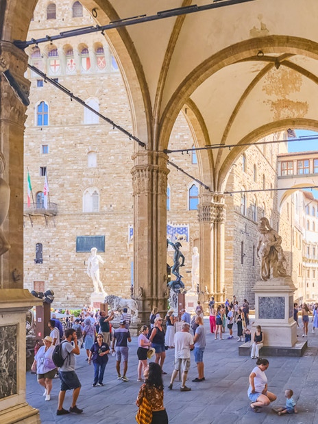 Tourists exploring statues at Loggia dei Lanzi near Palazzo Vecchio, Florence.