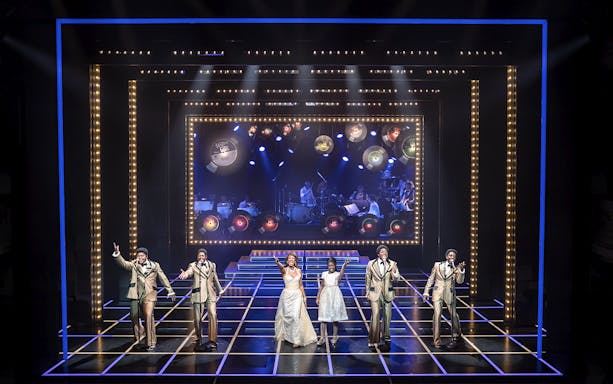 Performers on stage during "The Drifters Girl" musical with band in background.